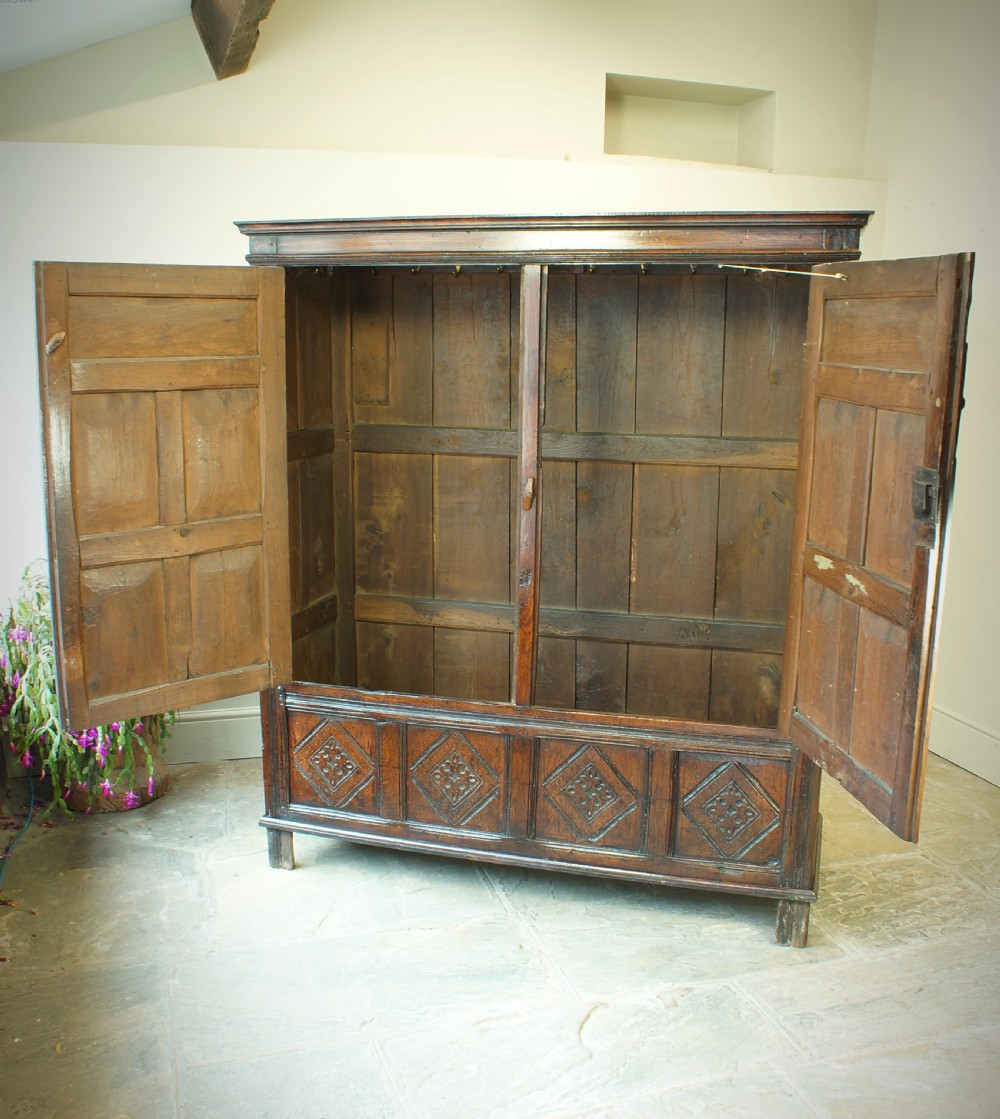 A dark brown seventeenth-century carved oak press cupboard featuring symmetrical panel doors and geometric detailing. View IX