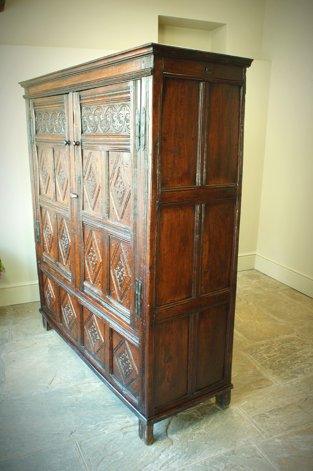 A dark brown seventeenth-century carved oak press cupboard featuring symmetrical panel doors and geometric detailing. View X