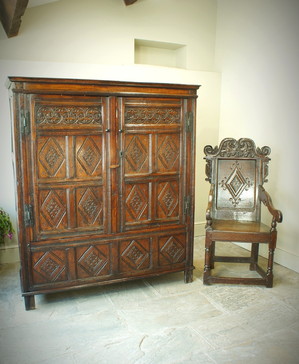 A dark brown seventeenth-century carved oak press cupboard featuring symmetrical panel doors and geometric detailing. View XI