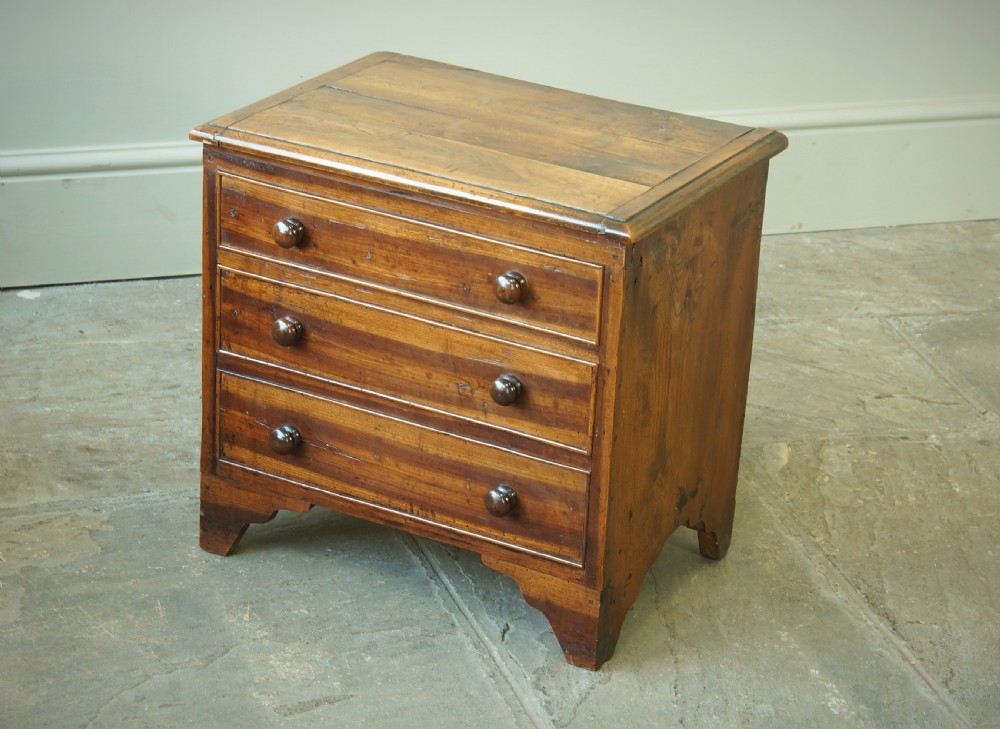 A Georgian plumwood close stool disguised as a small three-drawer chest with turned wooden knobs and bracket feet. View II