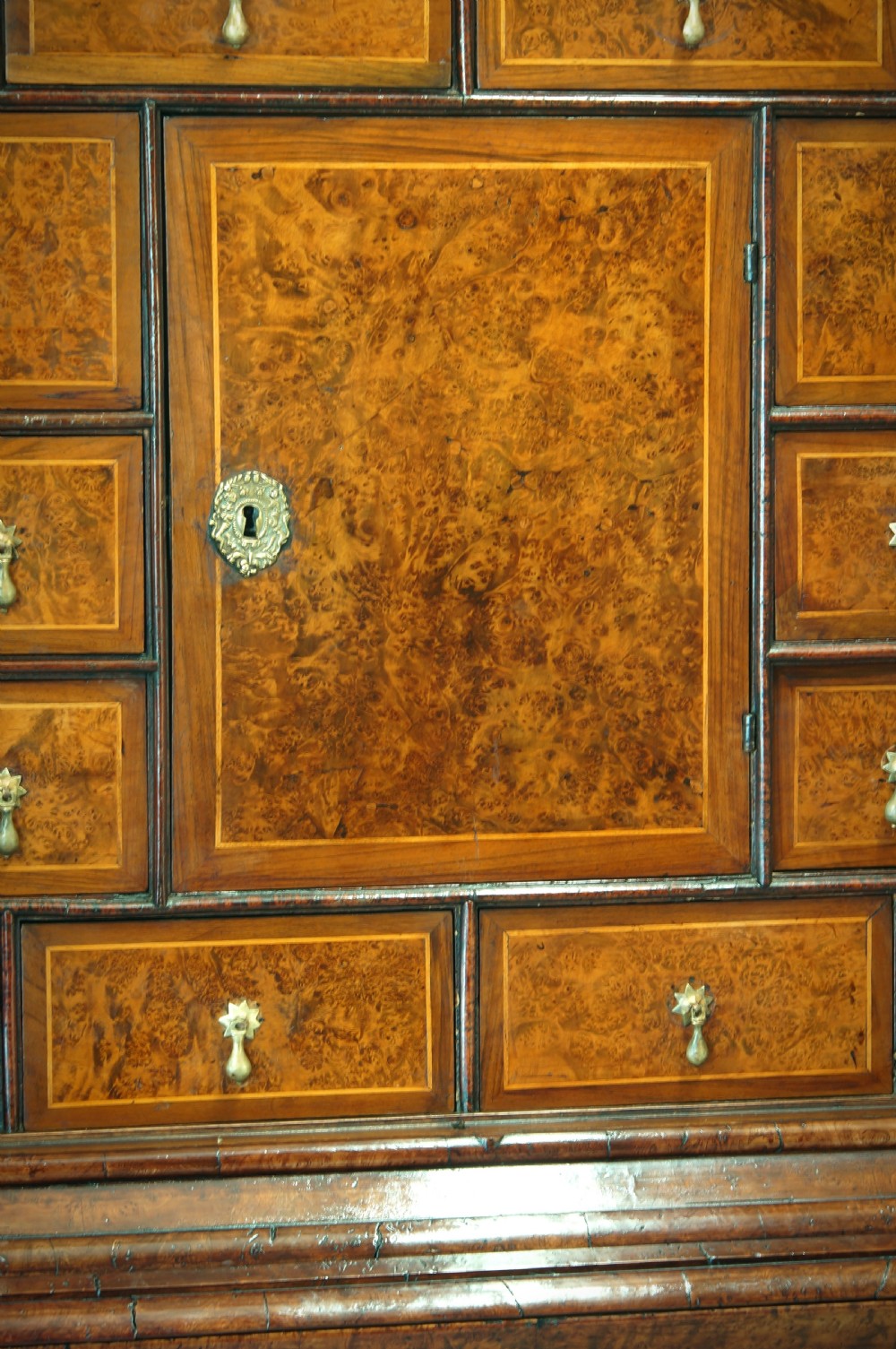 A William and Mary style cabinet on chest featuring double doors with burr amboyna wood veneers, brass keyhole escutcheons, multiple lower drawers, and compressed bun feet. View III