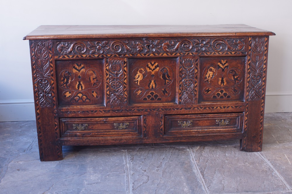 A 17th-century dark oak mule chest featuring carved friezes, three inlaid marquetry front panels with bird motifs, and two lower drawers with brass drop handles. View II