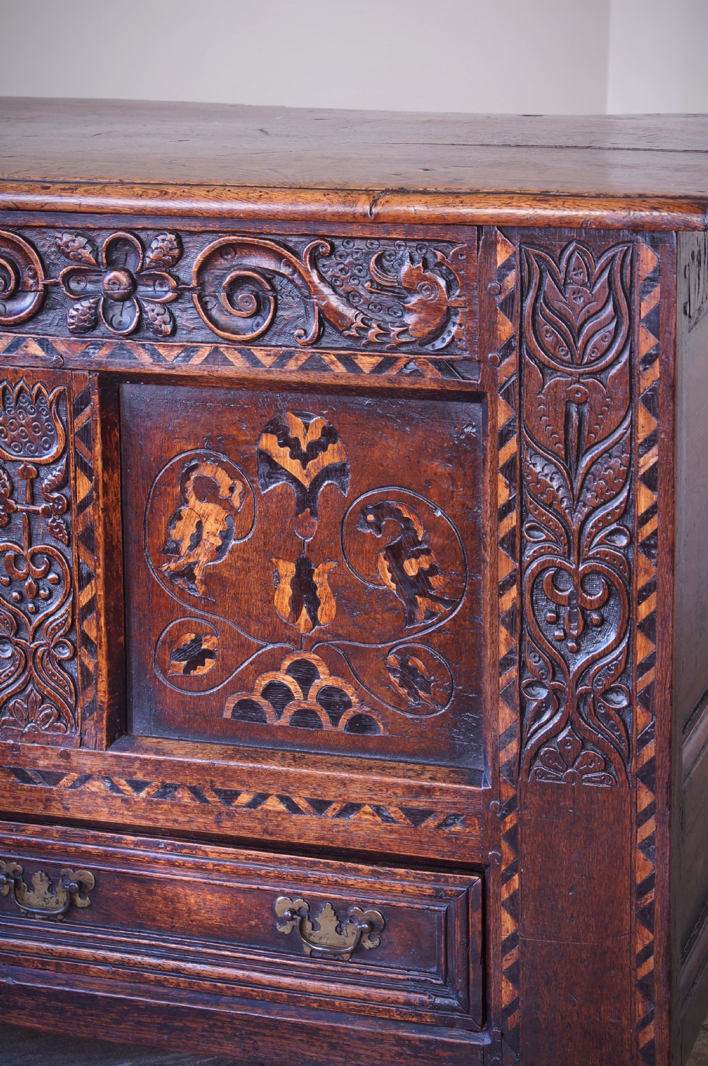 A 17th-century dark oak mule chest featuring carved friezes, three inlaid marquetry front panels with bird motifs, and two lower drawers with brass drop handles. View III
