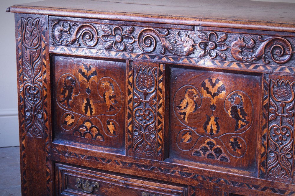 A 17th-century dark oak mule chest featuring carved friezes, three inlaid marquetry front panels with bird motifs, and two lower drawers with brass drop handles. View V