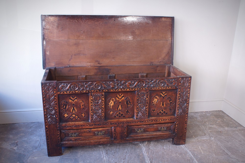 A 17th-century dark oak mule chest featuring carved friezes, three inlaid marquetry front panels with bird motifs, and two lower drawers with brass drop handles. View VII