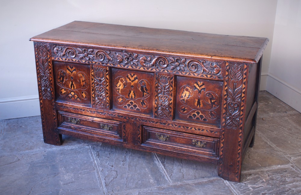 A 17th-century dark oak mule chest featuring carved friezes, three inlaid marquetry front panels with bird motifs, and two lower drawers with brass drop handles. View VIII