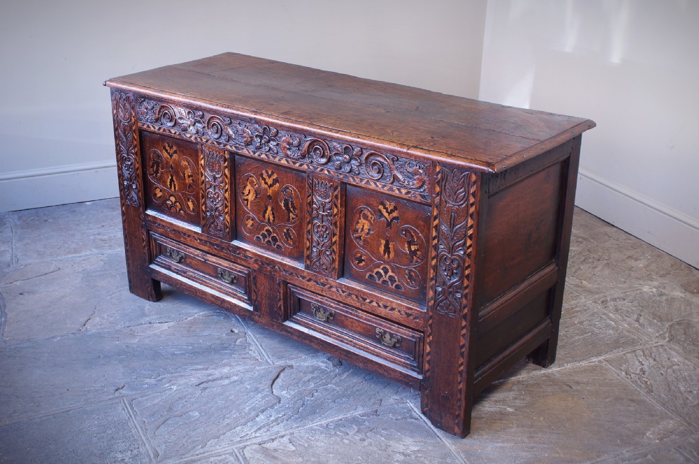 A 17th-century dark oak mule chest featuring carved friezes, three inlaid marquetry front panels with bird motifs, and two lower drawers with brass drop handles. View XII