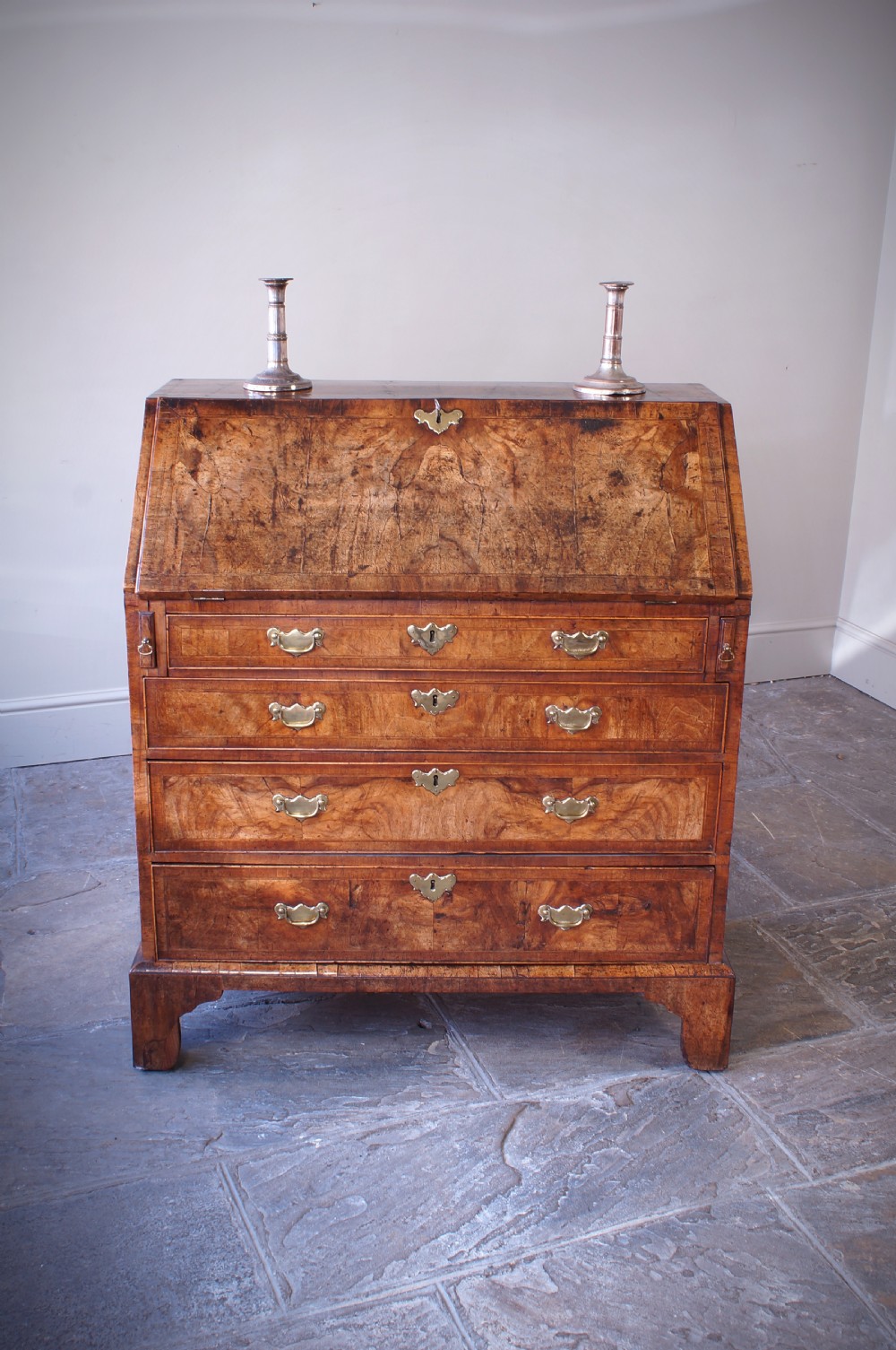 An 18th-century George II walnut bureau featuring a slant-front lid above four graduated drawers with brass handles, supported by bracket feet.