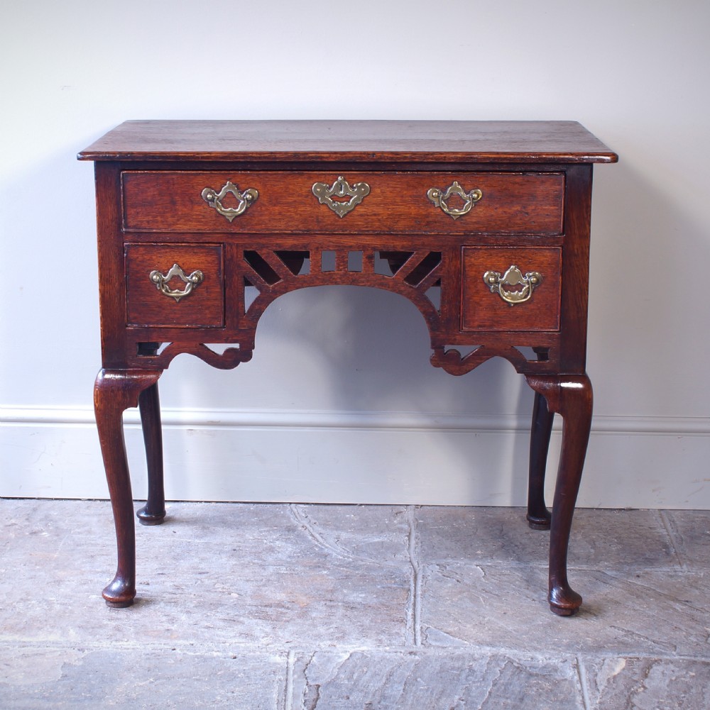 An 18th-century oak lowboy side table featuring cabriole legs, multiple drawers with brass swing handles, and an arched apron detail. View X