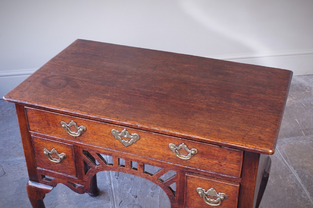 An 18th-century oak lowboy side table featuring cabriole legs, multiple drawers with brass swing handles, and an arched apron detail. View V