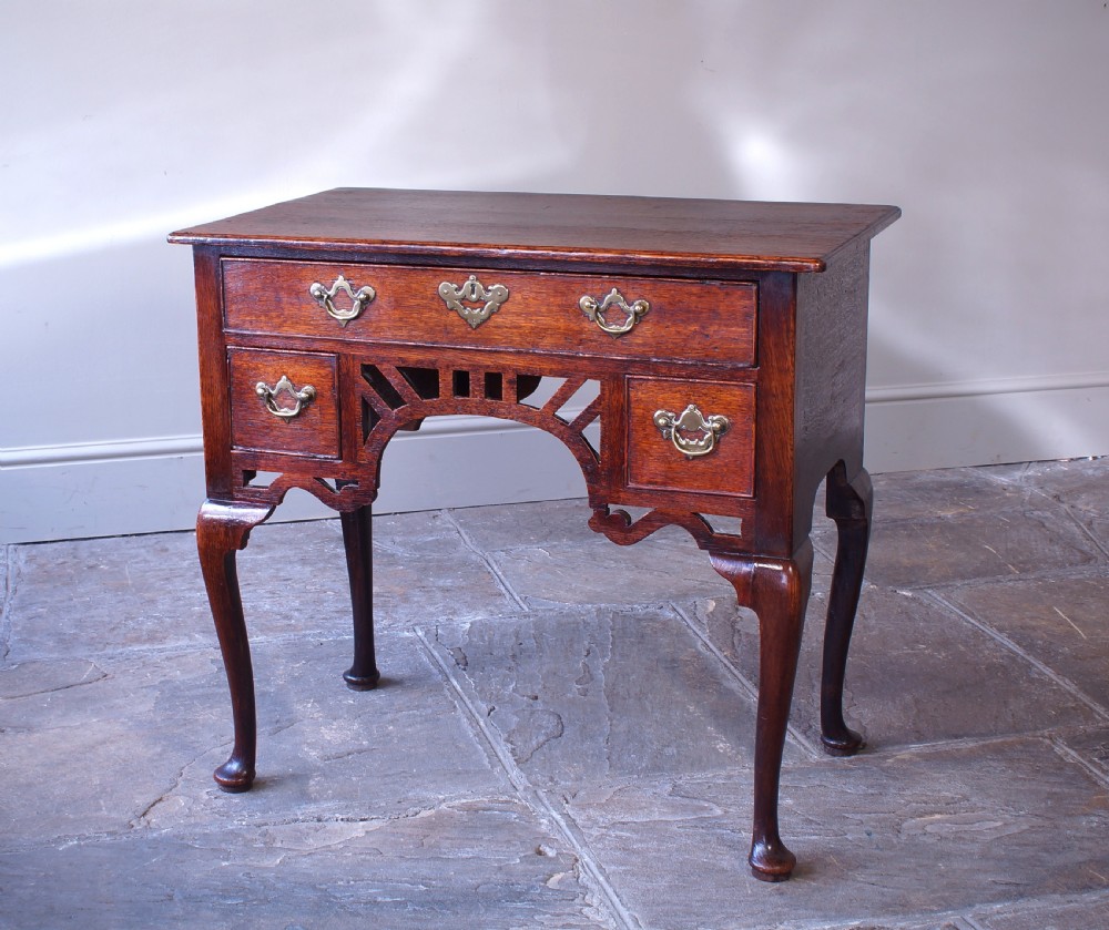 An 18th-century oak lowboy side table featuring cabriole legs, multiple drawers with brass swing handles, and an arched apron detail. View IX