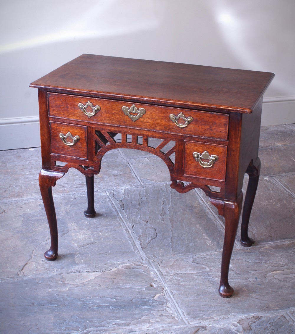 An 18th-century oak lowboy side table featuring cabriole legs, multiple drawers with brass swing handles, and an arched apron detail.