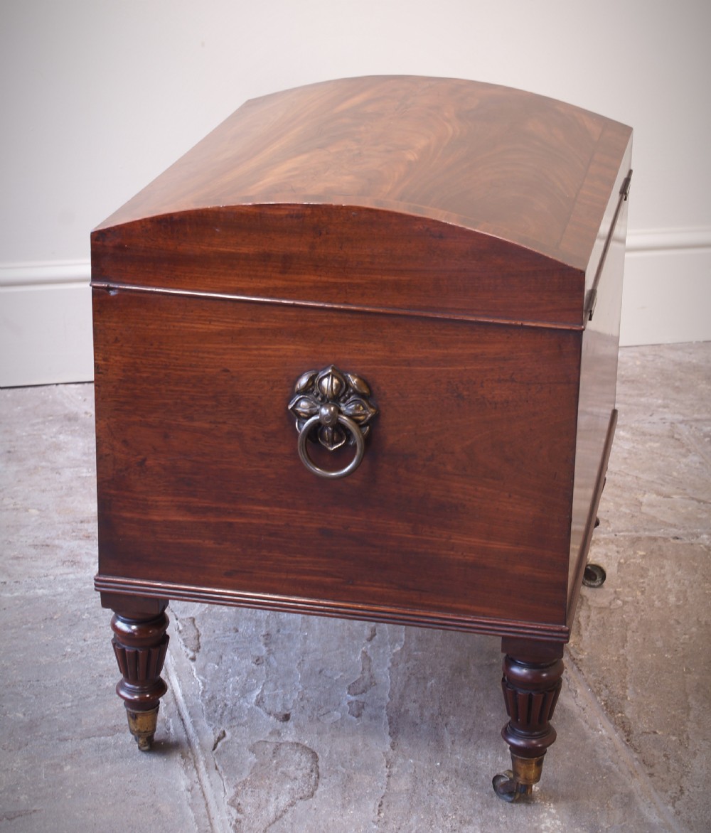 An open early 19th-century Regency flame mahogany cellarette featuring turned reeded legs, brass castors, side ring handles, and internal glass decanters. View VI