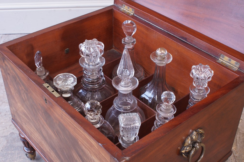 An open early 19th-century Regency flame mahogany cellarette featuring turned reeded legs, brass castors, side ring handles, and internal glass decanters. View IX