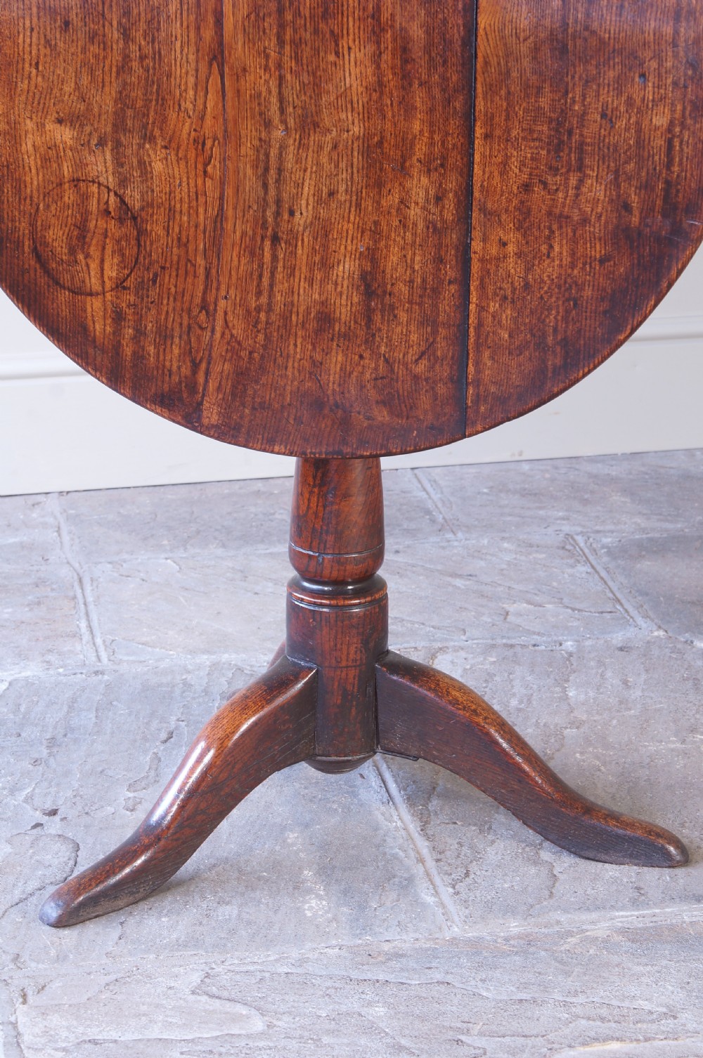 An 18th-century circular elm tilt-top tripod table shown with its top upright on a turned central column and three cabriole legs. View III