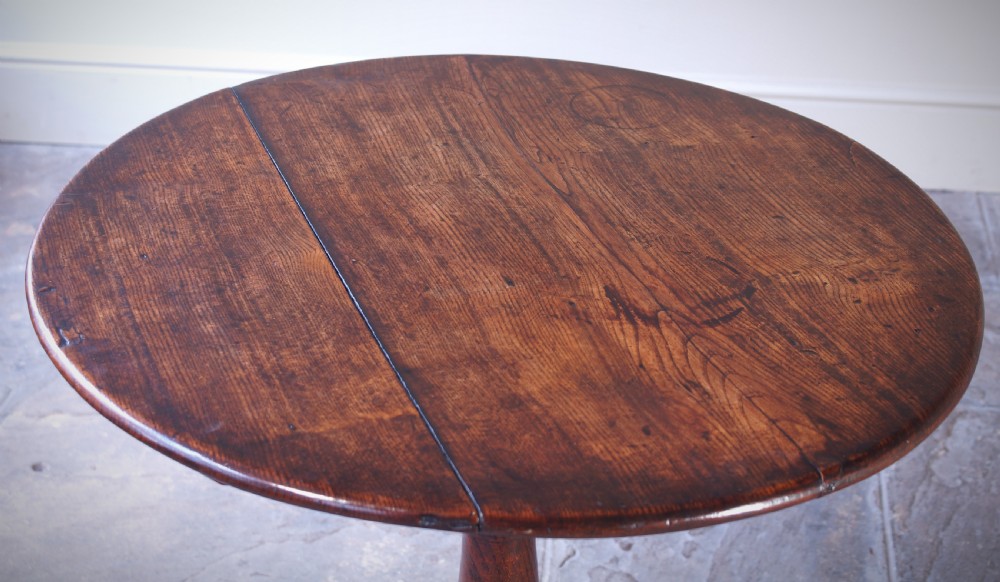 An 18th-century circular elm tilt-top tripod table shown with its top upright on a turned central column and three cabriole legs. View V