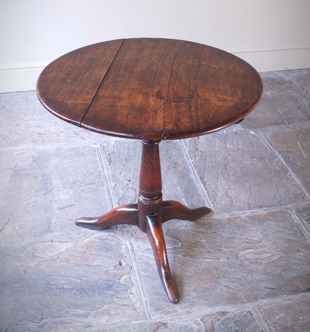 An 18th-century circular elm tilt-top tripod table shown with its top upright on a turned central column and three cabriole legs. View VII