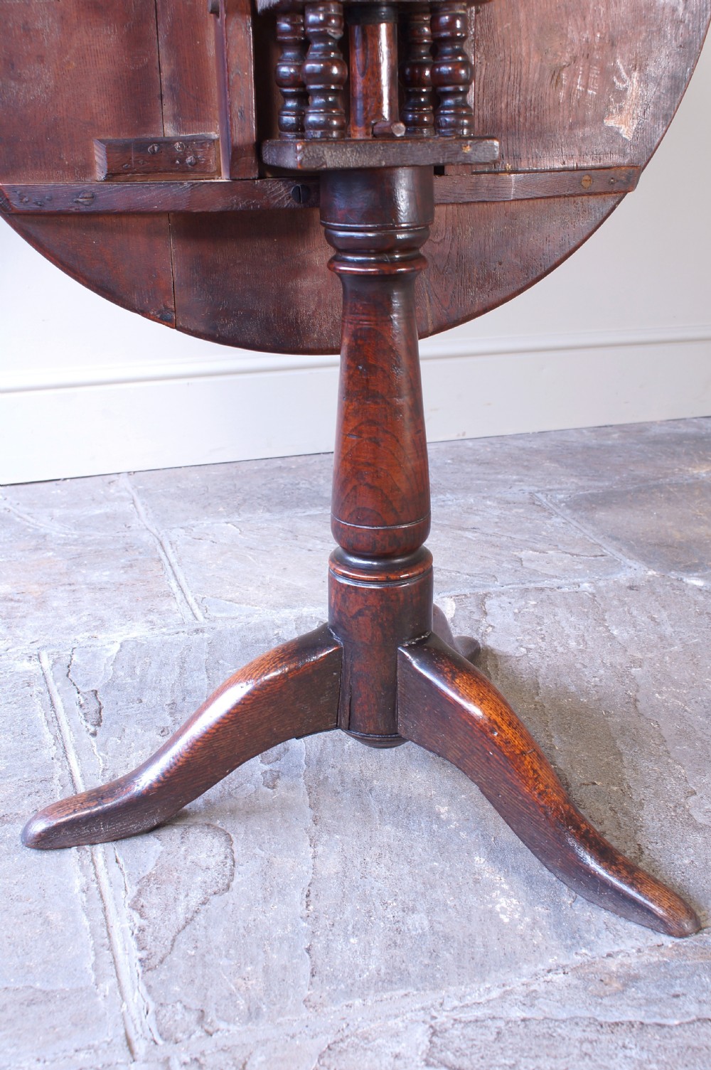 An 18th-century circular elm tilt-top tripod table shown with its top upright on a turned central column and three cabriole legs. View VIII