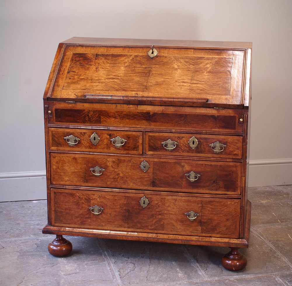 An early 18th-century walnut writing bureau featuring a sloping drop-front lid, brass drop handles, and turned bun feet. View VII