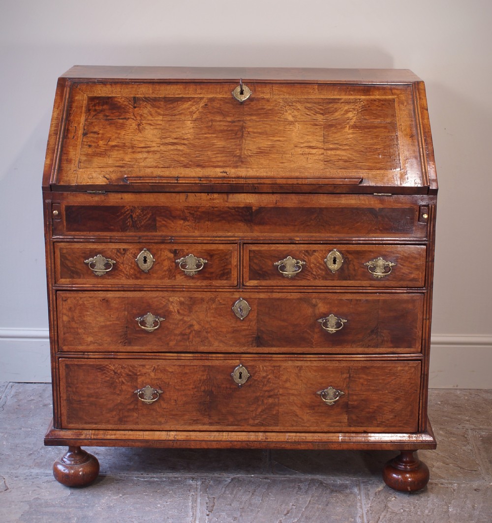 An early 18th-century walnut writing bureau featuring a sloping drop-front lid, brass drop handles, and turned bun feet. View III