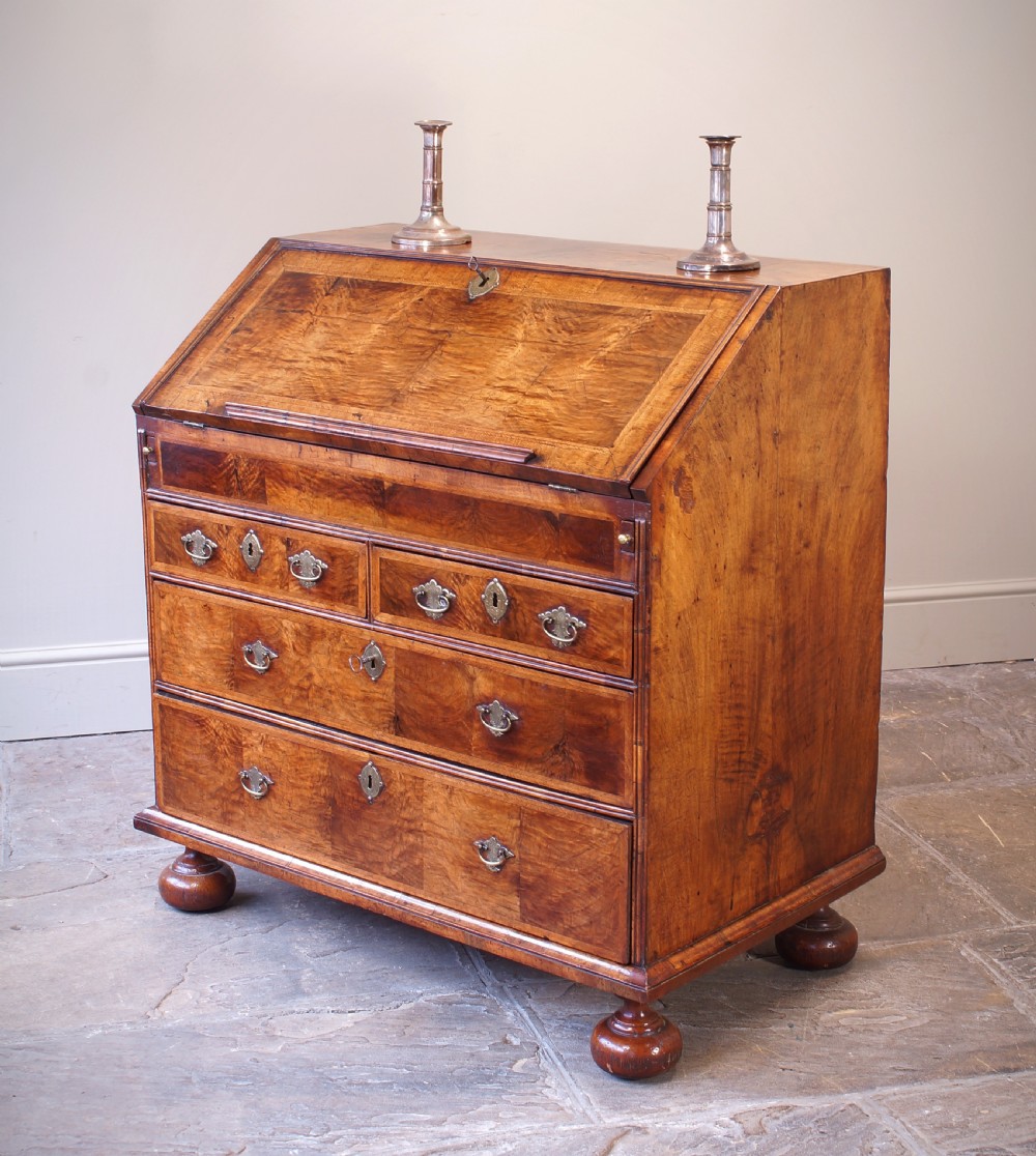 An early 18th-century walnut writing bureau featuring a sloping drop-front lid, brass drop handles, and turned bun feet. View V