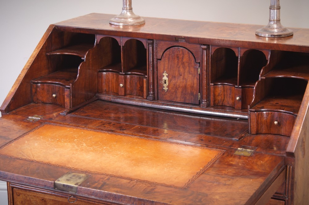 An early 18th-century walnut writing bureau featuring a sloping drop-front lid, brass drop handles, and turned bun feet. View IX