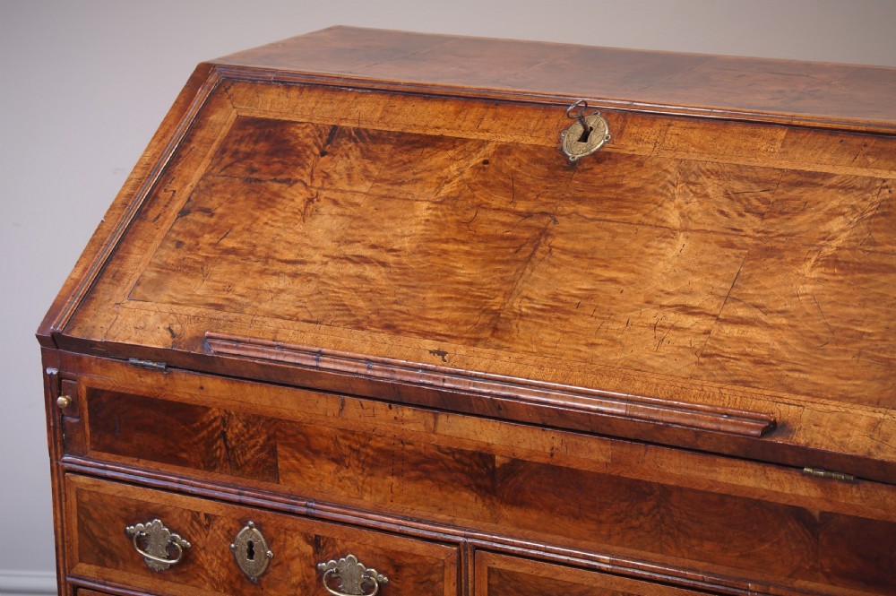 An early 18th-century walnut writing bureau featuring a sloping drop-front lid, brass drop handles, and turned bun feet. View X