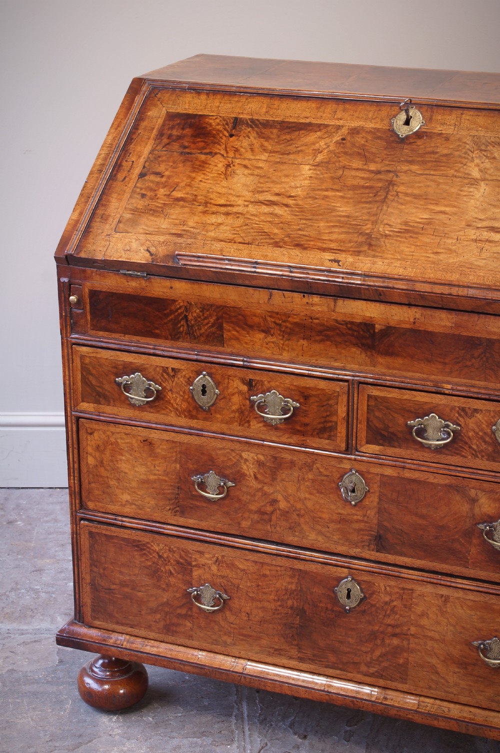 An early 18th-century walnut writing bureau featuring a sloping drop-front lid, brass drop handles, and turned bun feet. View XI