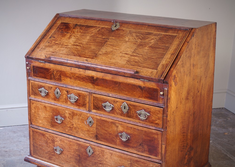 An early 18th-century walnut writing bureau featuring a sloping drop-front lid, brass drop handles, and turned bun feet. View XIV