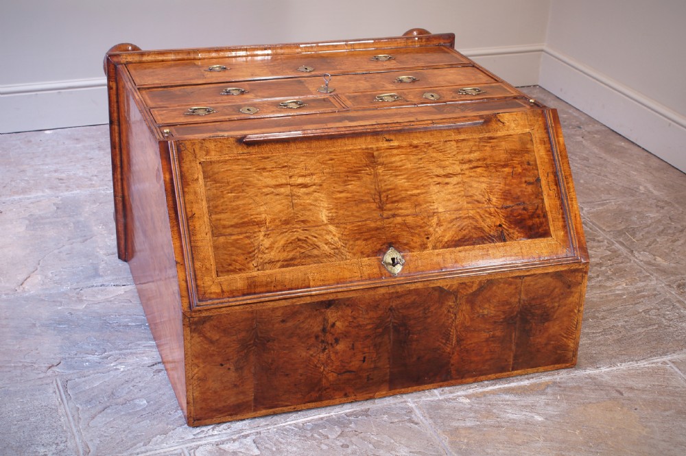An early 18th-century walnut writing bureau featuring a sloping drop-front lid, brass drop handles, and turned bun feet. View XVI