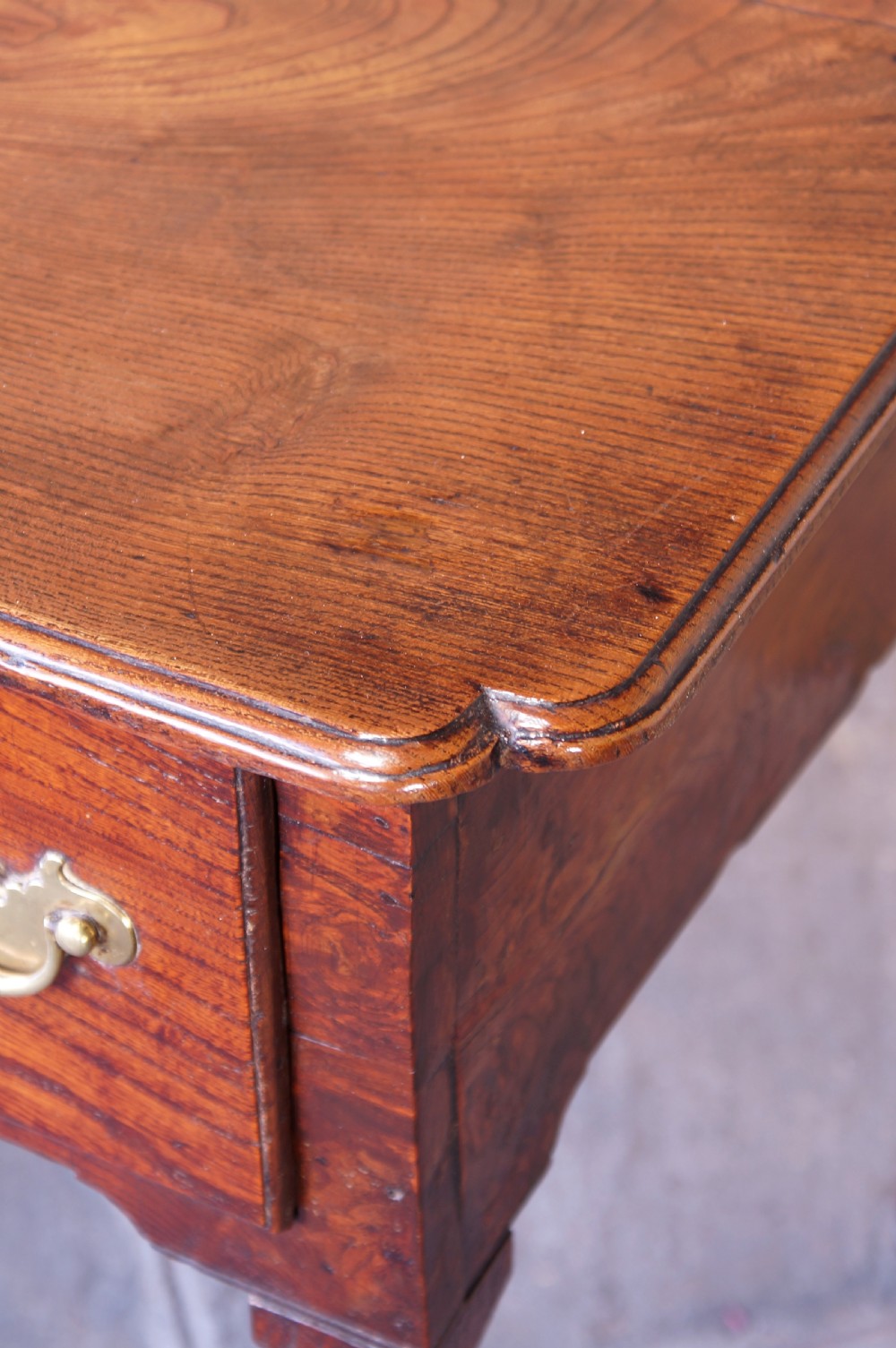 An 18th-century dark brown elm lowboy side table featuring three drawers with brass handles, a shaped apron, and four slender tapered legs ending in pad feet. View III