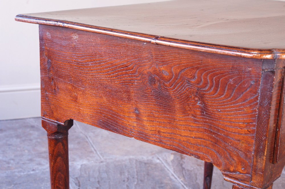 An 18th-century dark brown elm lowboy side table featuring three drawers with brass handles, a shaped apron, and four slender tapered legs ending in pad feet. View VI