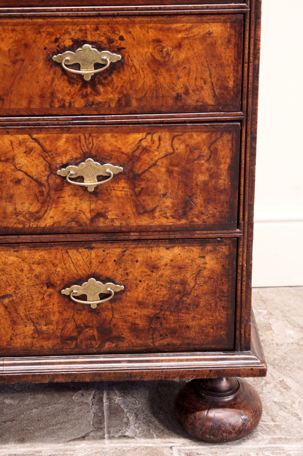 An early eighteenth-century burr walnut cabinet on chest featuring double upper doors with brass strap hinges above four graduated drawers, resting on turned bun feet. View V