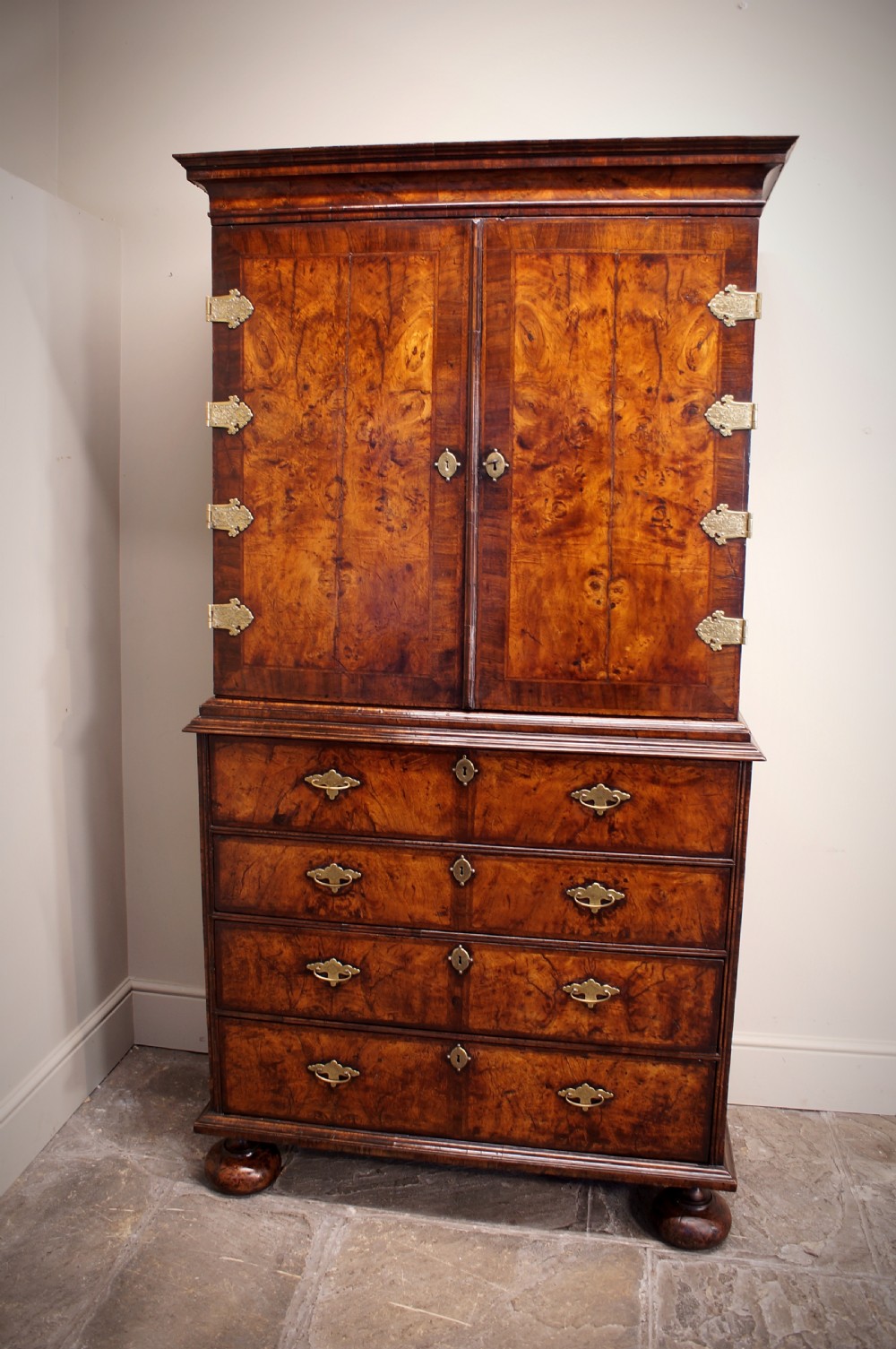 An early eighteenth-century burr walnut cabinet on chest featuring double upper doors with brass strap hinges above four graduated drawers, resting on turned bun feet. View XII