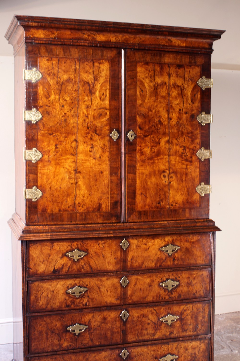 An early eighteenth-century burr walnut cabinet on chest featuring double upper doors with brass strap hinges above four graduated drawers, resting on turned bun feet. View XXIV