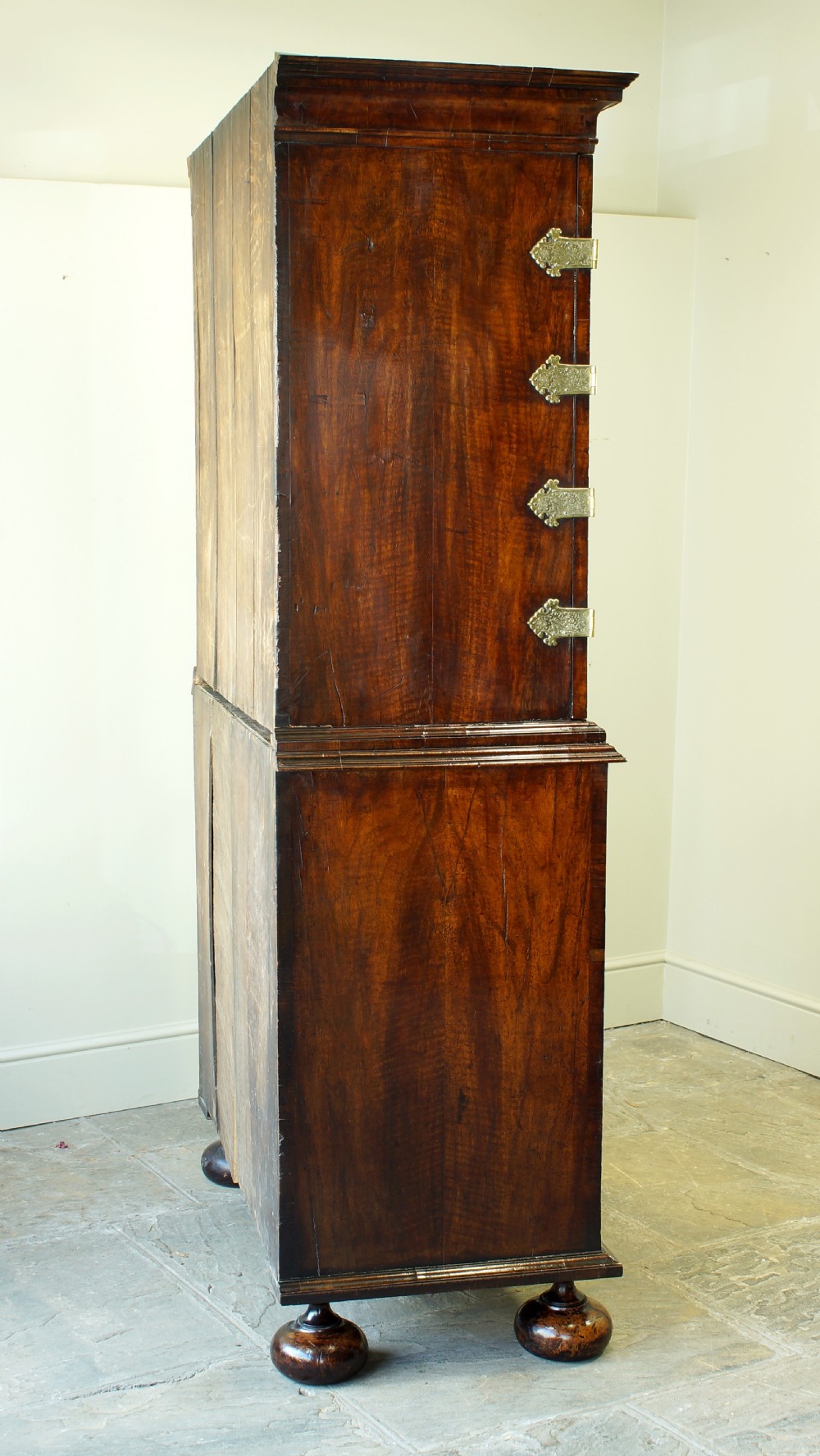 An early eighteenth-century burr walnut cabinet on chest featuring double upper doors with brass strap hinges above four graduated drawers, resting on turned bun feet. View XXIX