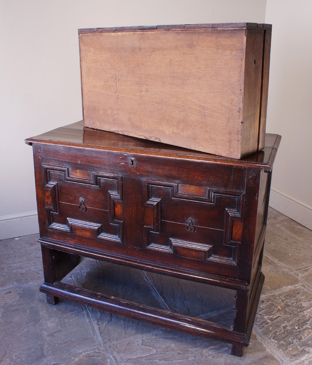 A seventeenth-century dark oak mule chest featuring raised geometric moulded panels on the front lid and two drawers below, set on short block feet. View II