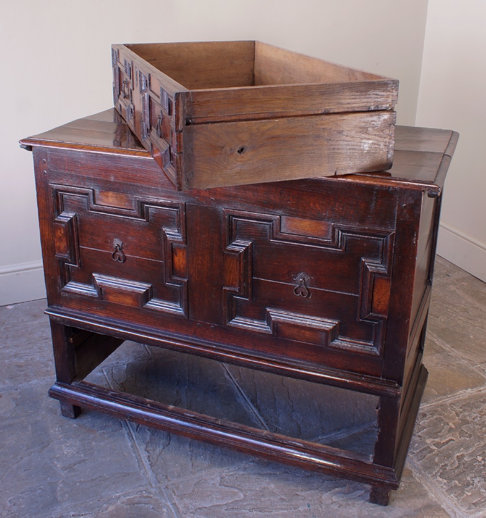 A seventeenth-century dark oak mule chest featuring raised geometric moulded panels on the front lid and two drawers below, set on short block feet. View III