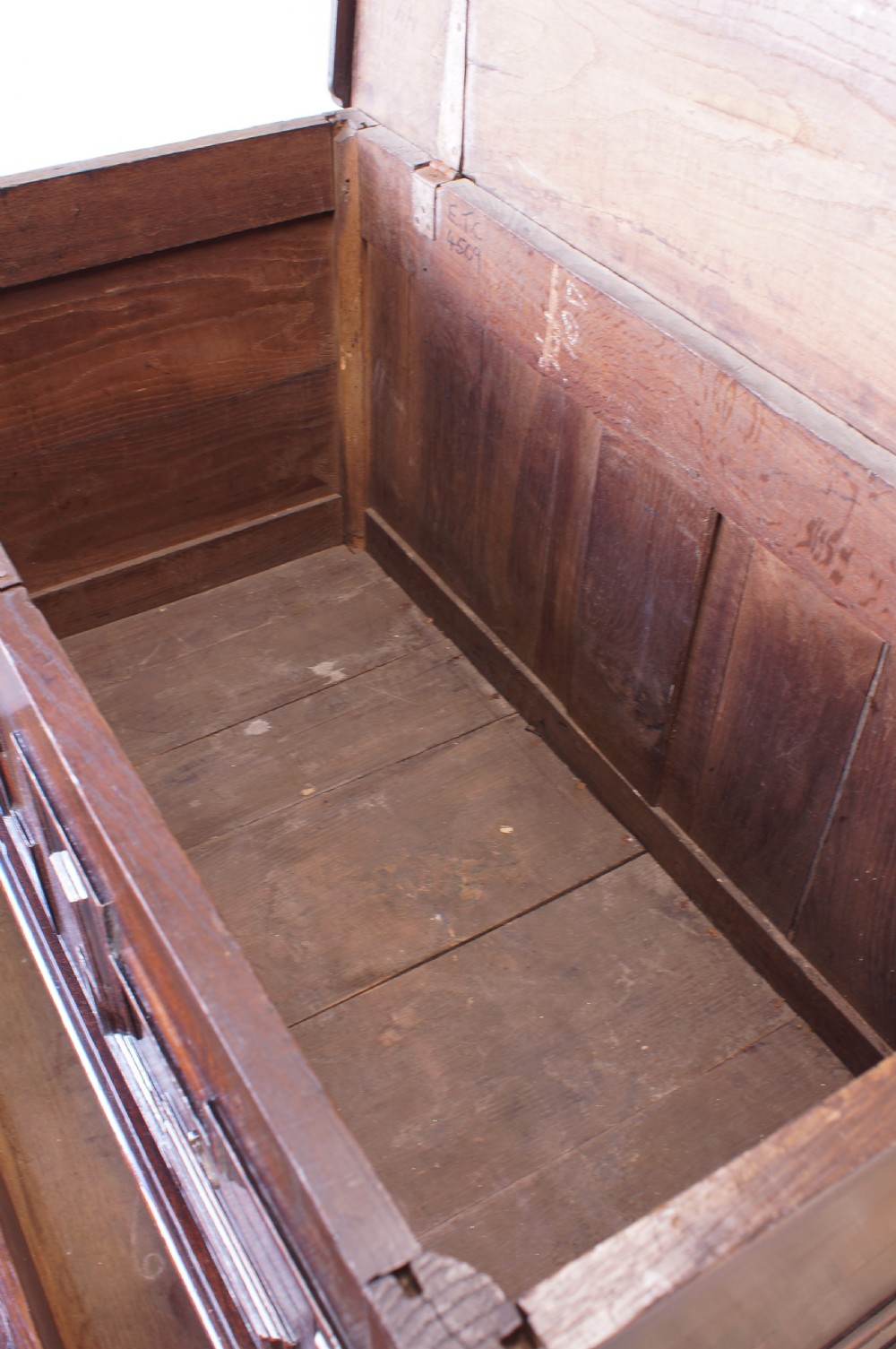 A seventeenth-century dark oak mule chest featuring raised geometric moulded panels on the front lid and two drawers below, set on short block feet. View V