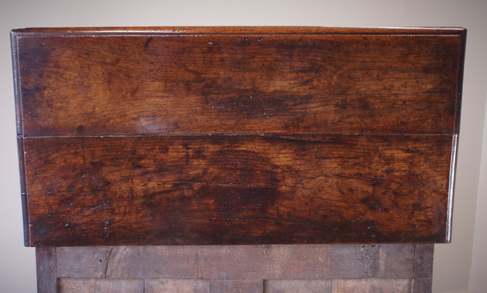 A seventeenth-century dark oak mule chest featuring raised geometric moulded panels on the front lid and two drawers below, set on short block feet. View VII