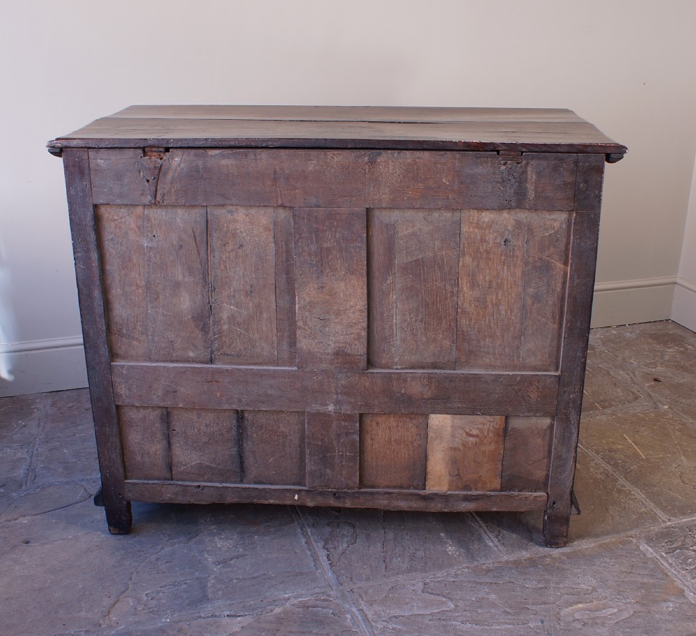 A seventeenth-century dark oak mule chest featuring raised geometric moulded panels on the front lid and two drawers below, set on short block feet. View VIII