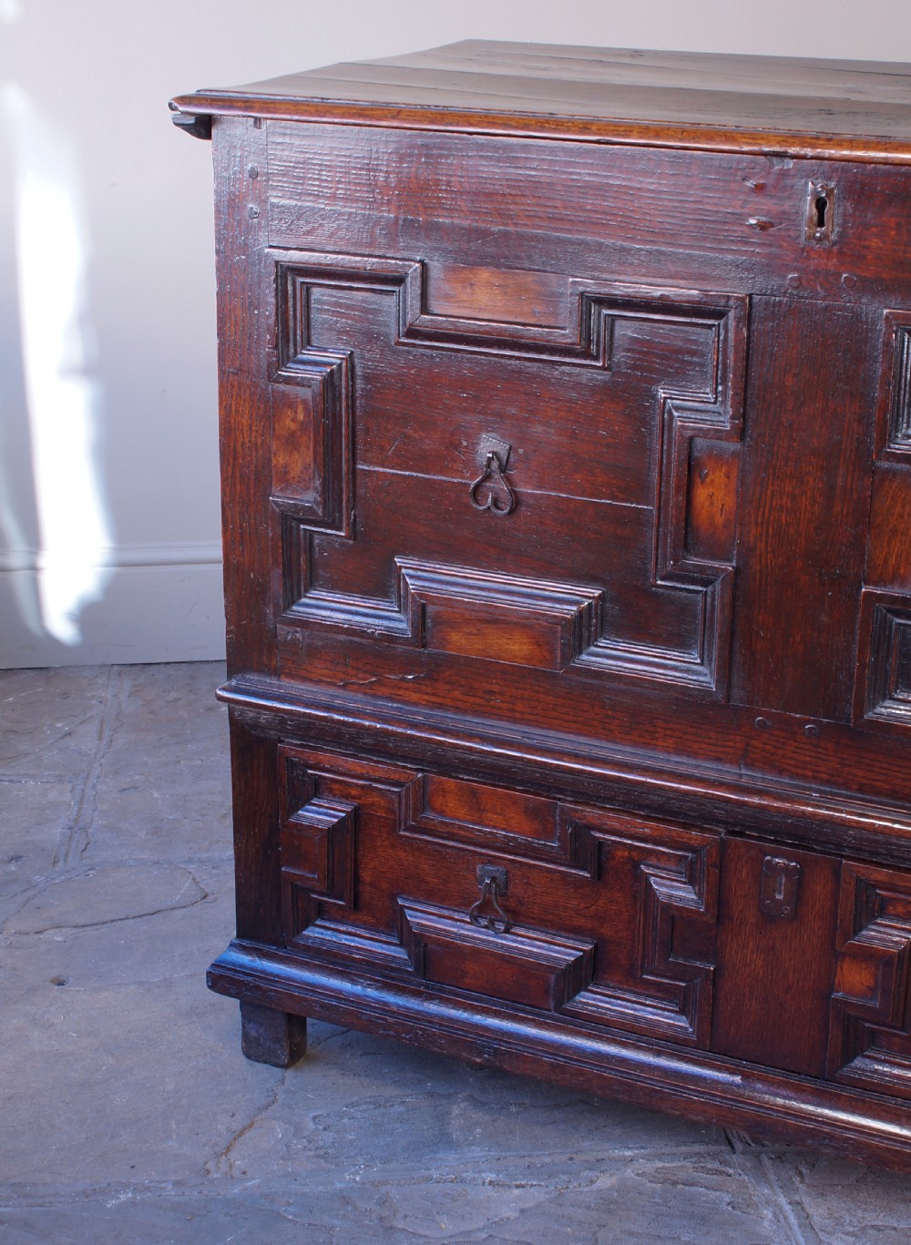 A seventeenth-century dark oak mule chest featuring raised geometric moulded panels on the front lid and two drawers below, set on short block feet. View IX