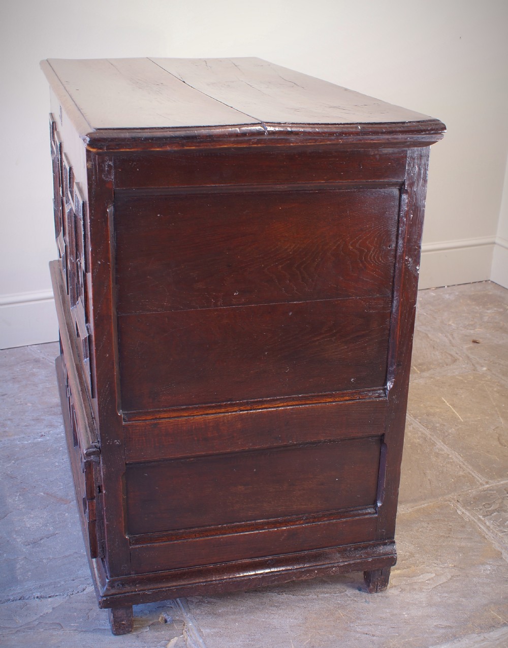 A seventeenth-century dark oak mule chest featuring raised geometric moulded panels on the front lid and two drawers below, set on short block feet. View X