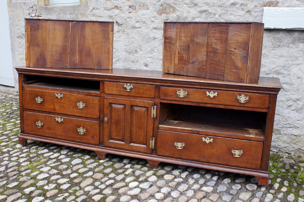 An 18th-century oak dresser base featuring multiple drawers, a central panelled cupboard door, brass handles, and bracket feet. View VIII