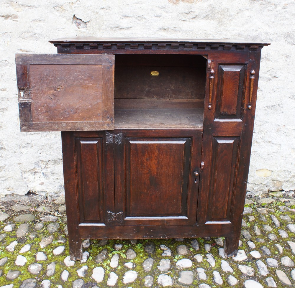 A dark oak 17th century hutch featuring panelled doors, hand-forged iron strap hinges, applied split turnings, and top edge dentil moulding. View IV