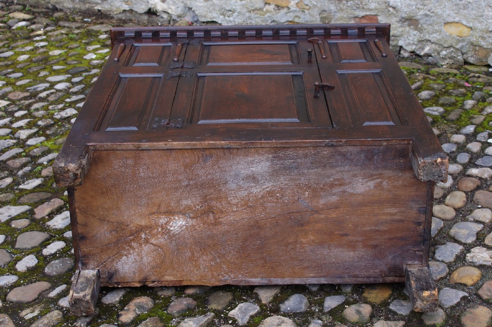 A dark oak 17th century hutch featuring panelled doors, hand-forged iron strap hinges, applied split turnings, and top edge dentil moulding. View IX
