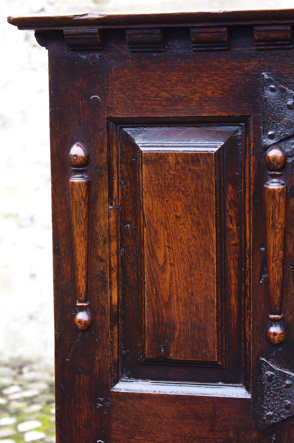 A dark oak 17th century hutch featuring panelled doors, hand-forged iron strap hinges, applied split turnings, and top edge dentil moulding. View X