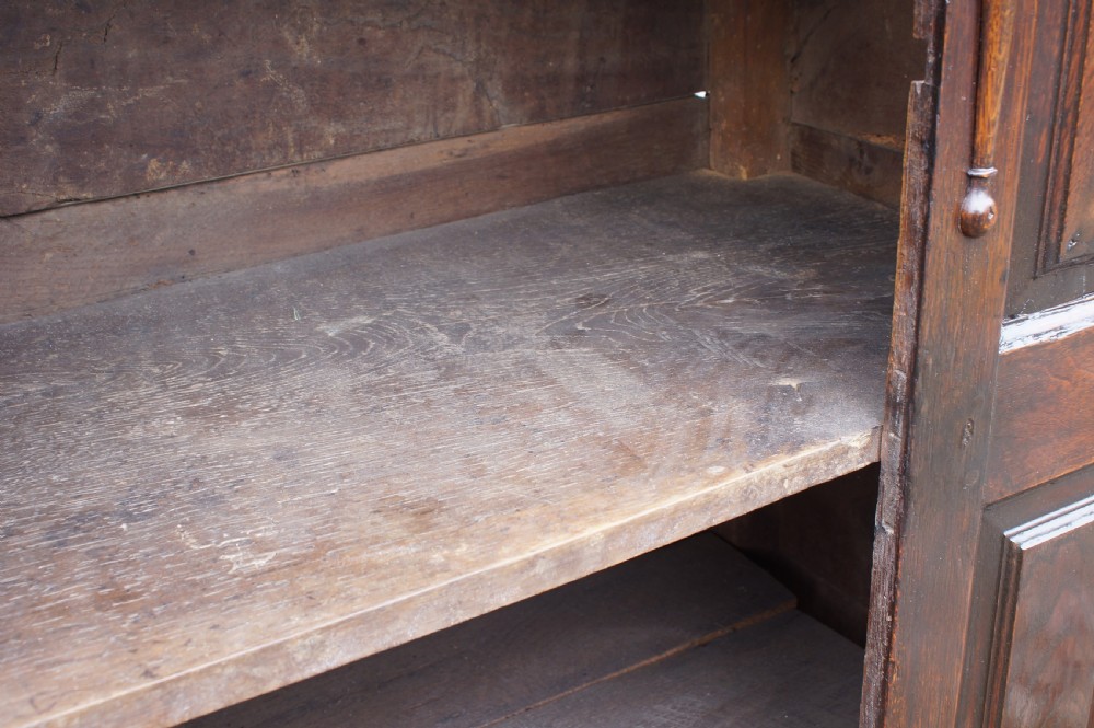 A dark oak 17th century hutch featuring panelled doors, hand-forged iron strap hinges, applied split turnings, and top edge dentil moulding. View XI