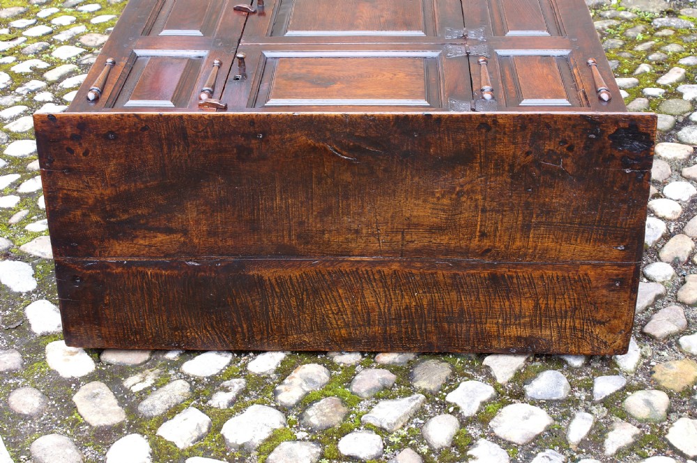 A dark oak 17th century hutch featuring panelled doors, hand-forged iron strap hinges, applied split turnings, and top edge dentil moulding. View XII