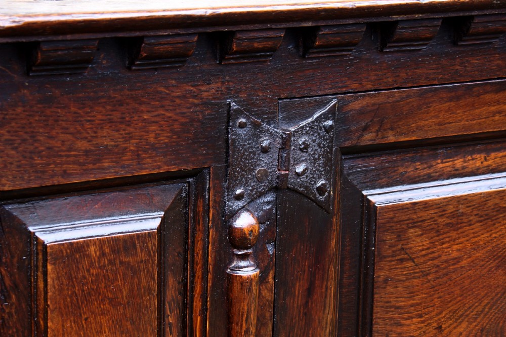 A dark oak 17th century hutch featuring panelled doors, hand-forged iron strap hinges, applied split turnings, and top edge dentil moulding. View XVI
